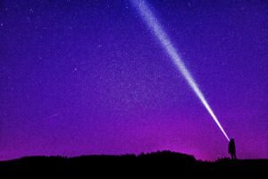 Silhouette of a person shining a flashlight under a starry violet night sky, creating a dramatic scene.